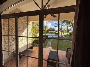 Vista a través de un ventanal de un patio con piscina, mobiliario exterior y un pabellón.