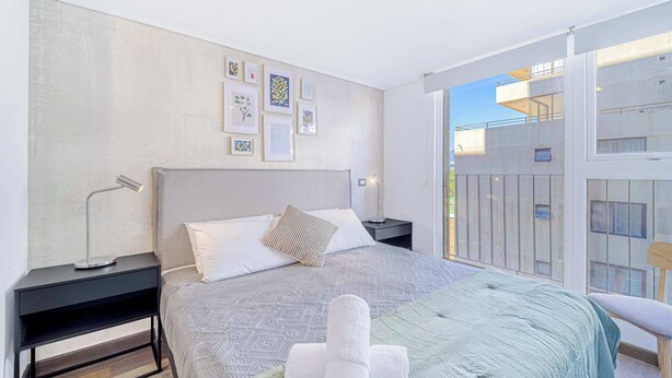 Ein modernes Schlafzimmer mit einem großen Bett, einem Nachttisch und einem Blick auf den Balkon.