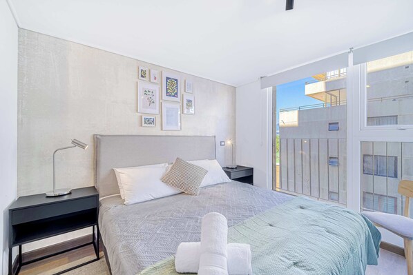 Un dormitorio moderno con una cama grande, una mesita de noche y vistas al balcón exterior.