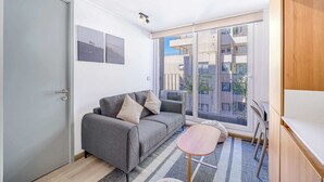 Ein modernes Wohnzimmer mit grauem Sofa, einem kleinen Holztisch und einer großen Glasschiebetür, die auf einen Balkon im Freien führt.