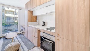 Eine moderne Küche mit Holzschränken, einer weißen Arbeitsplatte, einem eingebauten Ofen und einem Fenster mit Blick auf einen Balkon.