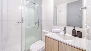 Ein modernes Badezimmer mit einer Duschkabine, einer weißen Toilette und einem Waschtisch mit Spiegel und Waschbecken.