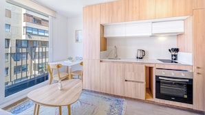 A modern kitchen with wooden cabinets, a built-in oven, and a dining area with a table and chairs. - Espacio Coventry II - 1D Wifi y AC (Ñuñoa)