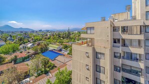 A high-rise building with multiple balconies, a rooftop terrace, and a view of a cityscape with mountains in the distance. - Espacio Coventry II - 1D Wifi y AC (Ñuñoa)