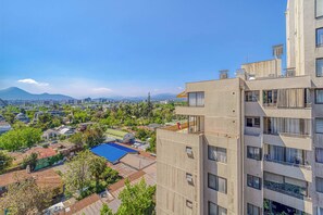 A high-rise building with multiple balconies, a rooftop terrace, and a view of a cityscape with mountains in the distance. - Espacio Coventry II - 1D Wifi y AC (Ñuñoa)