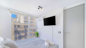 A modern bedroom with a large bed, a flat-screen TV mounted on the wall, and a sliding door. - Espacio Coventry II - 1D Wifi y AC (Ñuñoa)