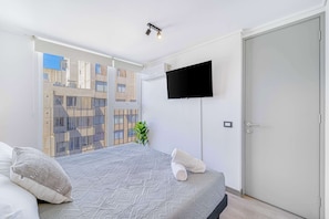 A modern bedroom with a large bed, a flat-screen TV mounted on the wall, and a sliding door. - Espacio Coventry II - 1D Wifi y AC (Ñuñoa)
