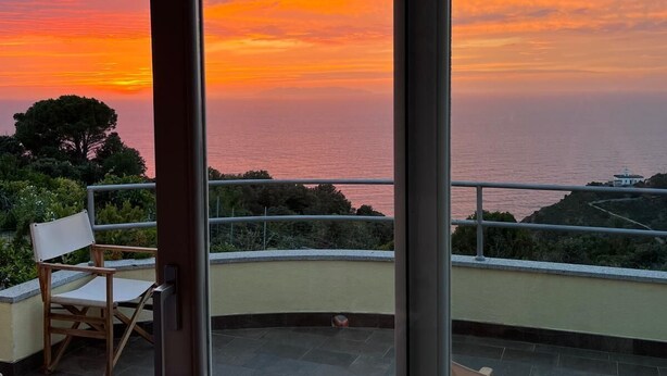 A balcony with a view of the sunset over the ocean, two folding chairs, and a railing. - Villa tre fari all'Isola d'Elba (Colle D'orano)