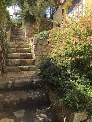 A stone staircase leading up to a building with a stone wall and greenery.