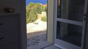 A room with a bed, a dresser, and a sliding glass door leading to a balcony with a view of the sea and greenery. - Villa tre fari all'Isola d'Elba (Colle D'orano)