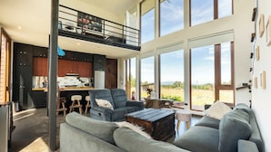 Amplia sala de estar con techo alto, cocina integrada y grandes ventanas que ofrecen vistas al exterior.