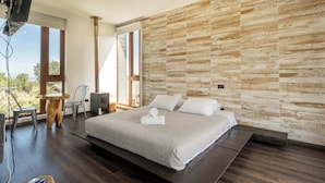 Un dormitorio con una cama grande, piso de madera, televisión y vistas al exterior.