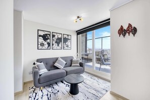 A modern living room with a grey sofa, a round coffee table, and a large window offering a city view. - Espacio Urbano- 3D, Vista 180° w/ Wifi (Ñuñoa)
