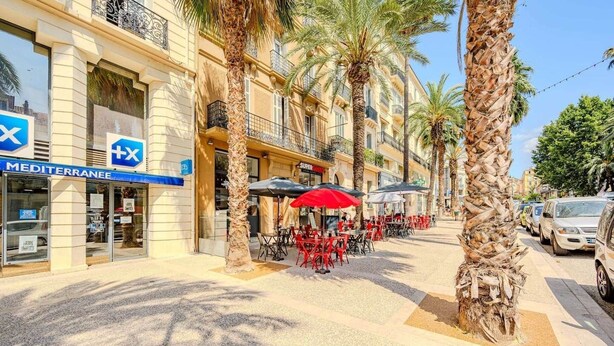 A Mediterranean-style street with outdoor seating, palm trees, and a 'MEDITERRANEAN' sign. - Bright, modern 2-bedroom in city center (Hyères)