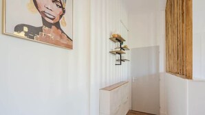A narrow hallway with a wooden floor, white walls, and a painting on the left. There are shelves with items on the right wall. - Bright, modern 2-bedroom in city center (Hyères)