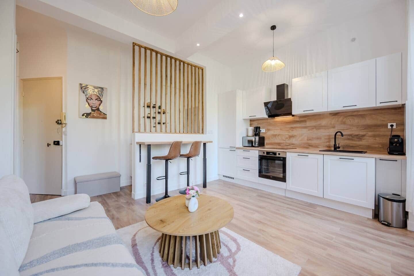 A modern kitchen with white cabinets, a wooden countertop, and a built-in oven. There is a dining area with a round wooden table and two chairs.