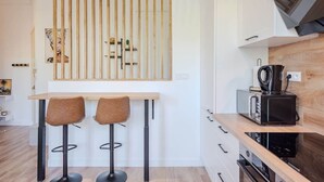 A modern kitchen with a wooden bar counter, two stools, and a coffee machine. - Bright, modern 2-bedroom in city center (Hyères)