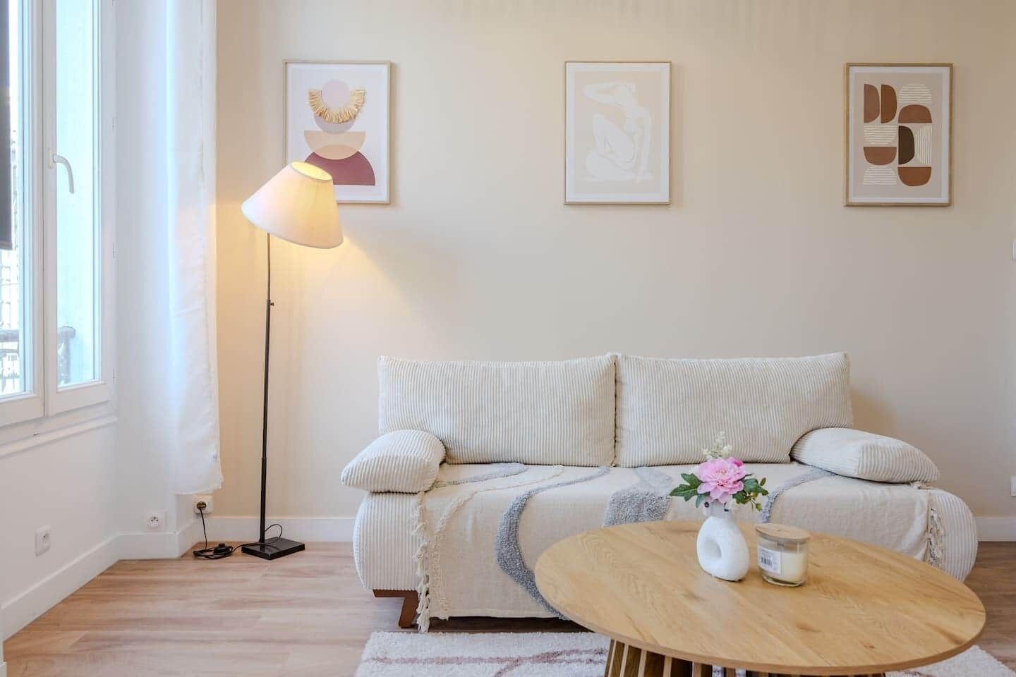 Un salon chaleureux avec un canapé, une lampe sur pied et des œuvres d’art encadrées accrochées au mur.