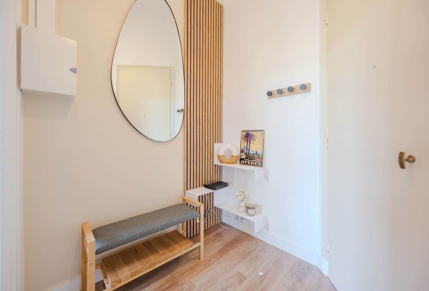 A minimalist bathroom with a bench, a mirror, a towel rack, and a shelf with toiletries.