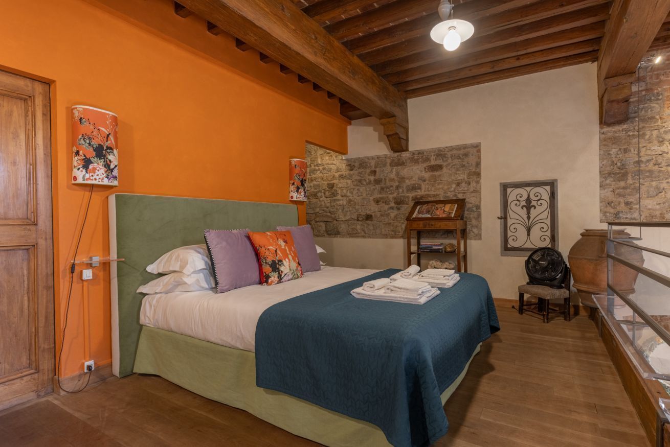 A bedroom with a bed, wooden beams, a stone wall, and a fan.