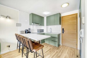 A compact kitchen with a white countertop, green cabinets, and a wooden door.