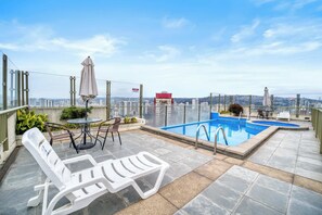 A rooftop pool area with lounge chairs, a table, and umbrellas.