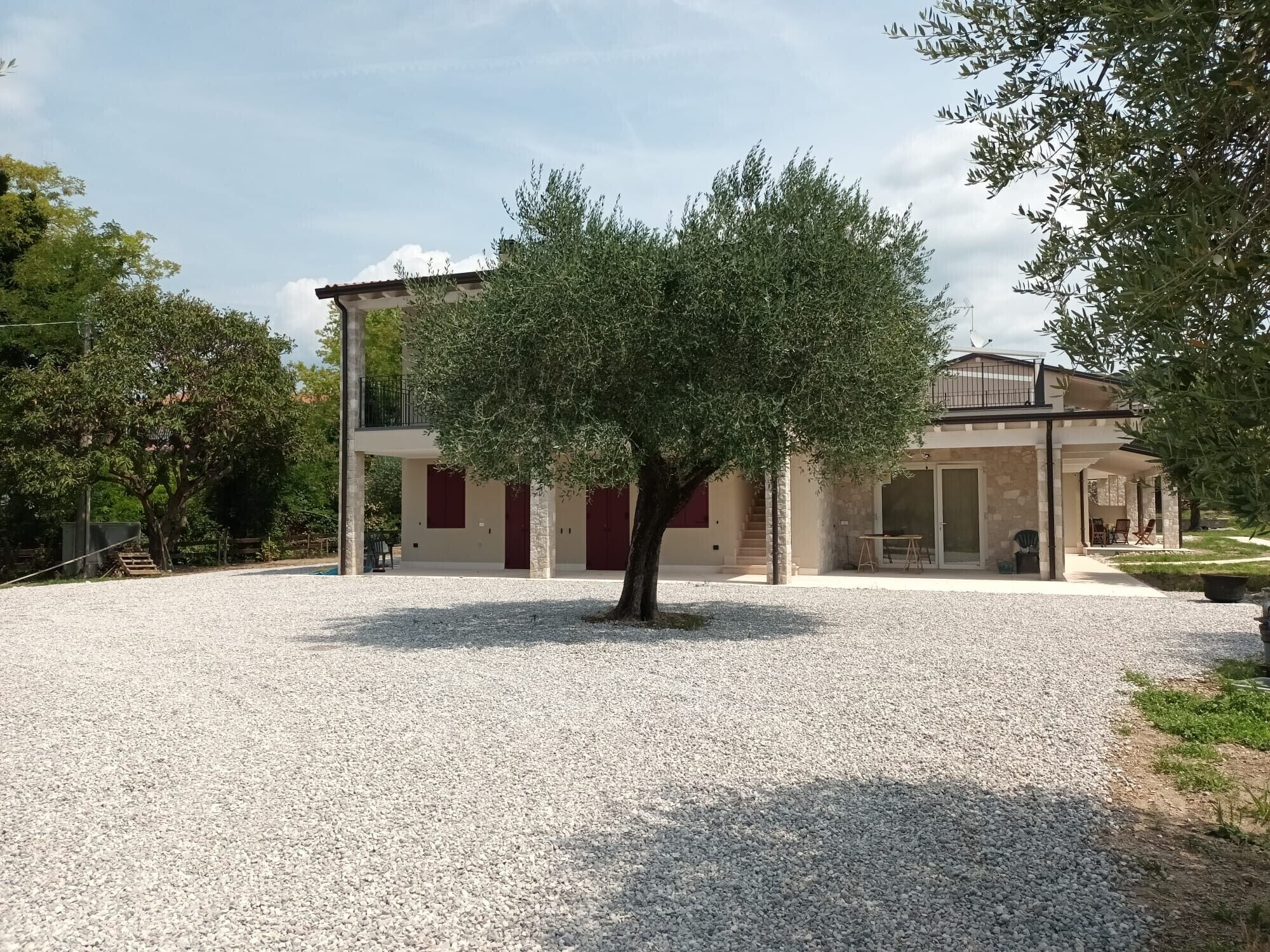 Un bâtiment avec une allée gravillonnée, un arbre au centre et un espace extérieur aménagé avec des sièges, protégé par un auvent.