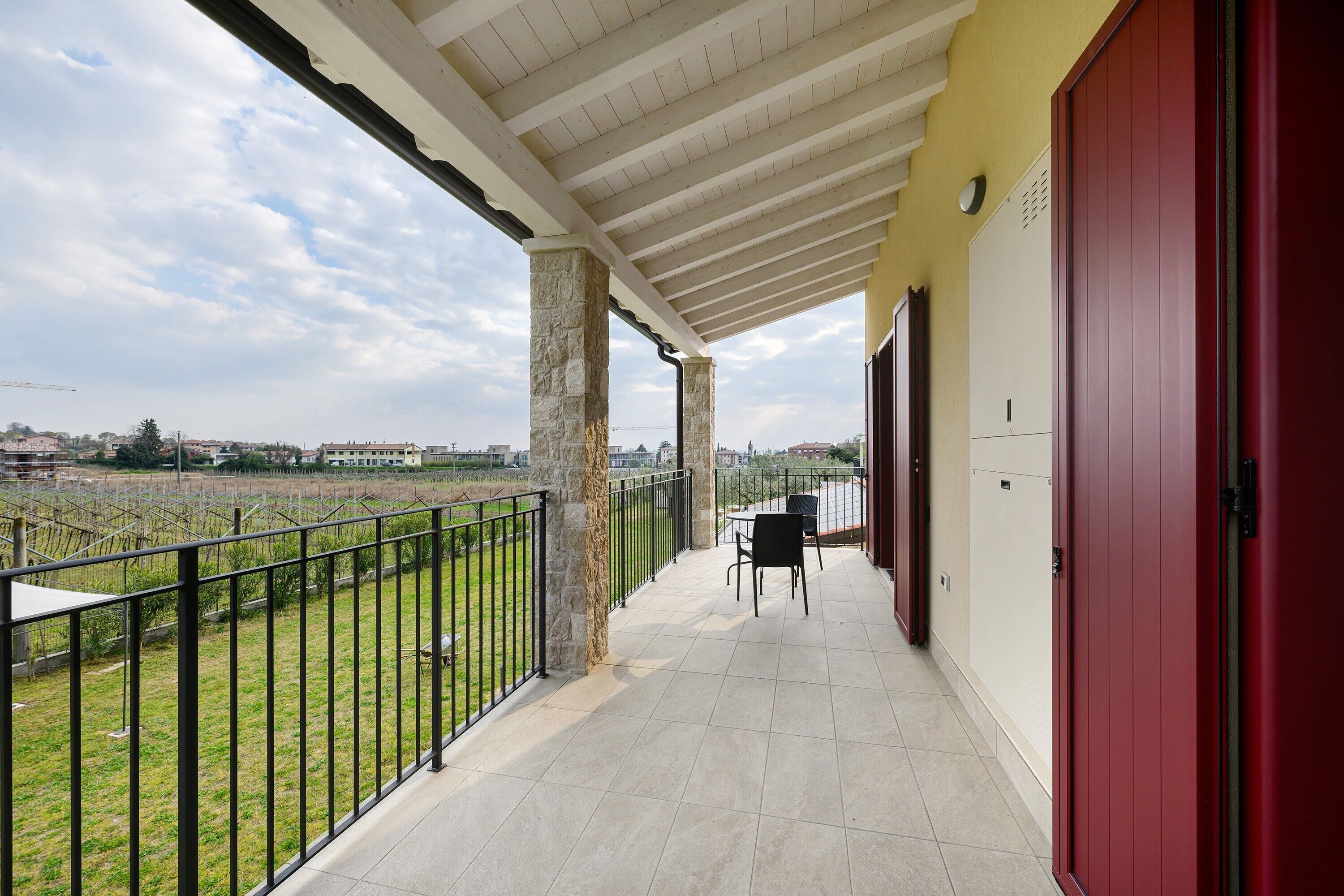 A balcony with a view of a vineyard, a red door, and a tiled floor.
