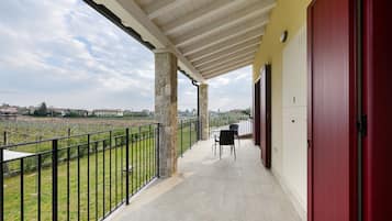 A balcony with a view of a vineyard, a red door, and a tiled floor.