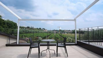 A balcony with a table and chairs, a view of a green landscape, and a clear sky.