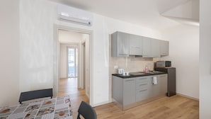 Una cocina moderna con armarios grises, un microondas y un refrigerador. Hay una mesa de comedor con mantel estampado y una silla.