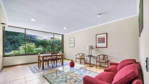 A spacious living room with a large window, a red sofa, a glass coffee table, and a dining area with chairs and a table. - Las Condes Urban Apartment W/ Wifi and Pool (Las Condes)