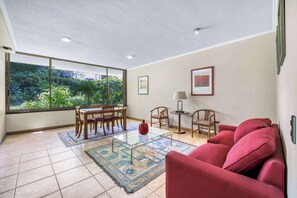 Amplia sala de estar con un ventanal grande, un sofá rojo, una mesa de centro de cristal y un comedor con sillas y una mesa.