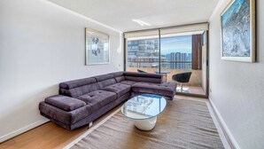 A modern living room with a sectional sofa, a glass coffee table, and a view of the city through large windows. - Las Condes Urban Apartment W/ Wifi and Pool (Las Condes)