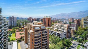 A high-rise residential building with multiple balconies, surrounded by other high-rise buildings and greenery. - Las Condes Urban Apartment W/ Wifi and Pool (Las Condes)