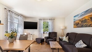 A modern living room with a wooden dining table, a sofa, a chair, and a flat-screen TV mounted on the wall. - Apartment 'Beim Häusler' with Wi-Fi (Radibor)