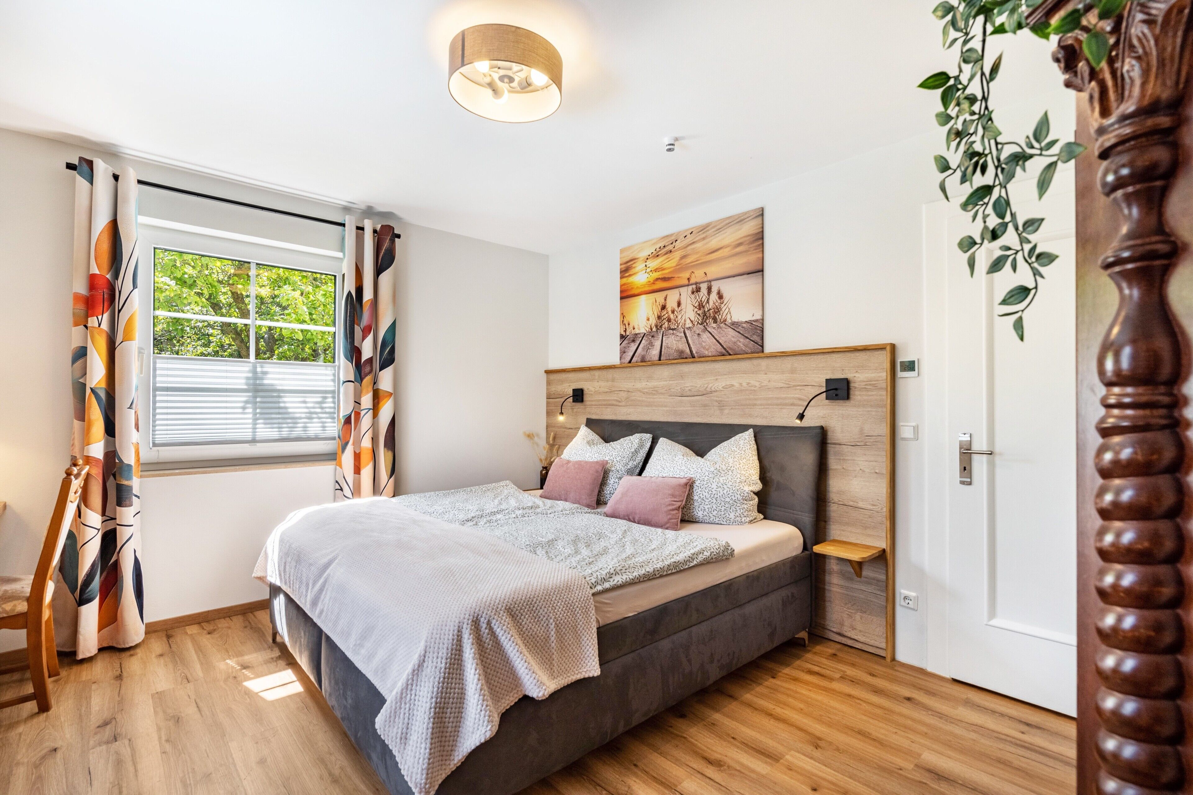 Ein Schlafzimmer mit Bett, Vorhängen, einem Fenster, einem Gemälde und Holzboden.
