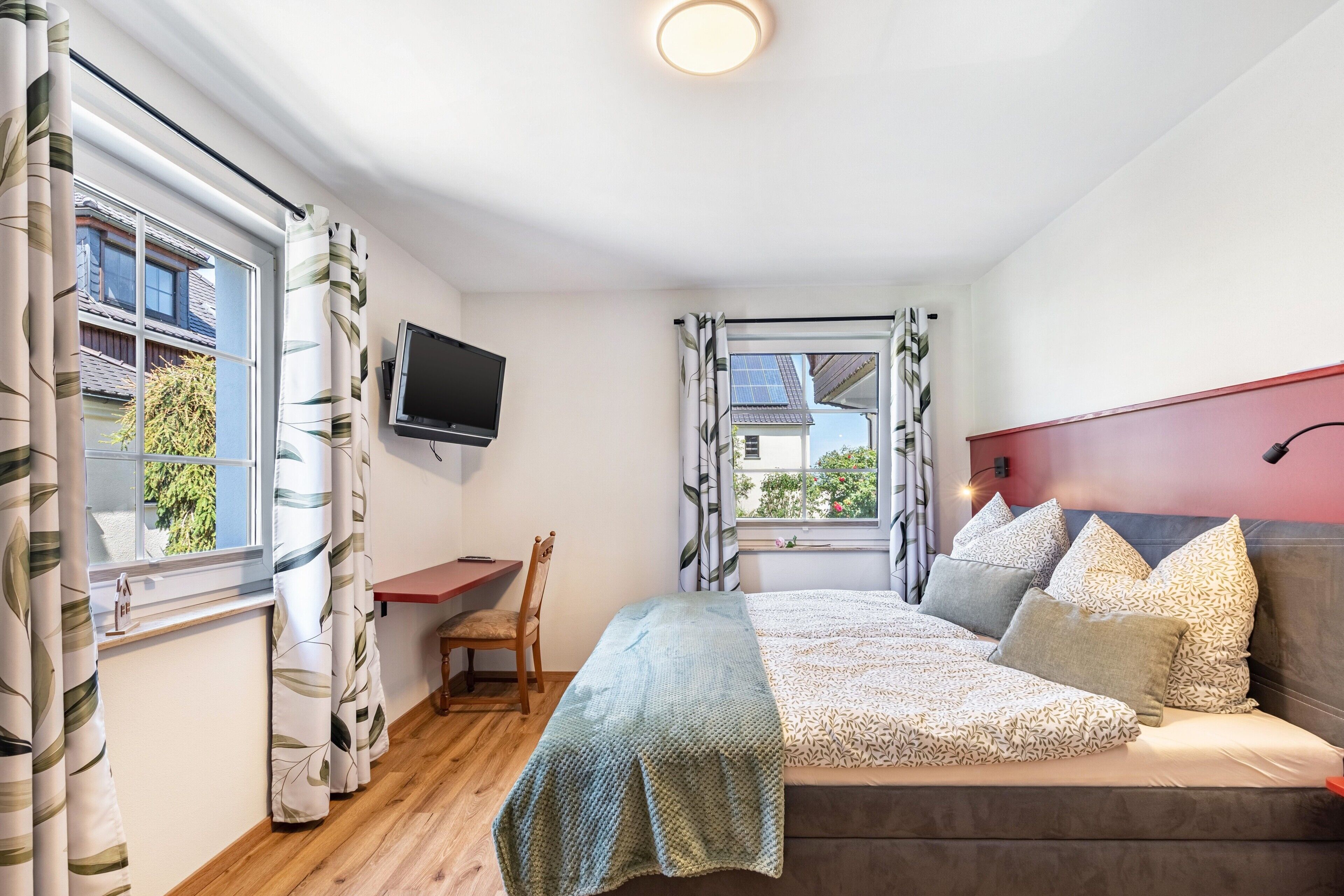A bedroom with a bed, a desk, a chair, a television, and a window with curtains.