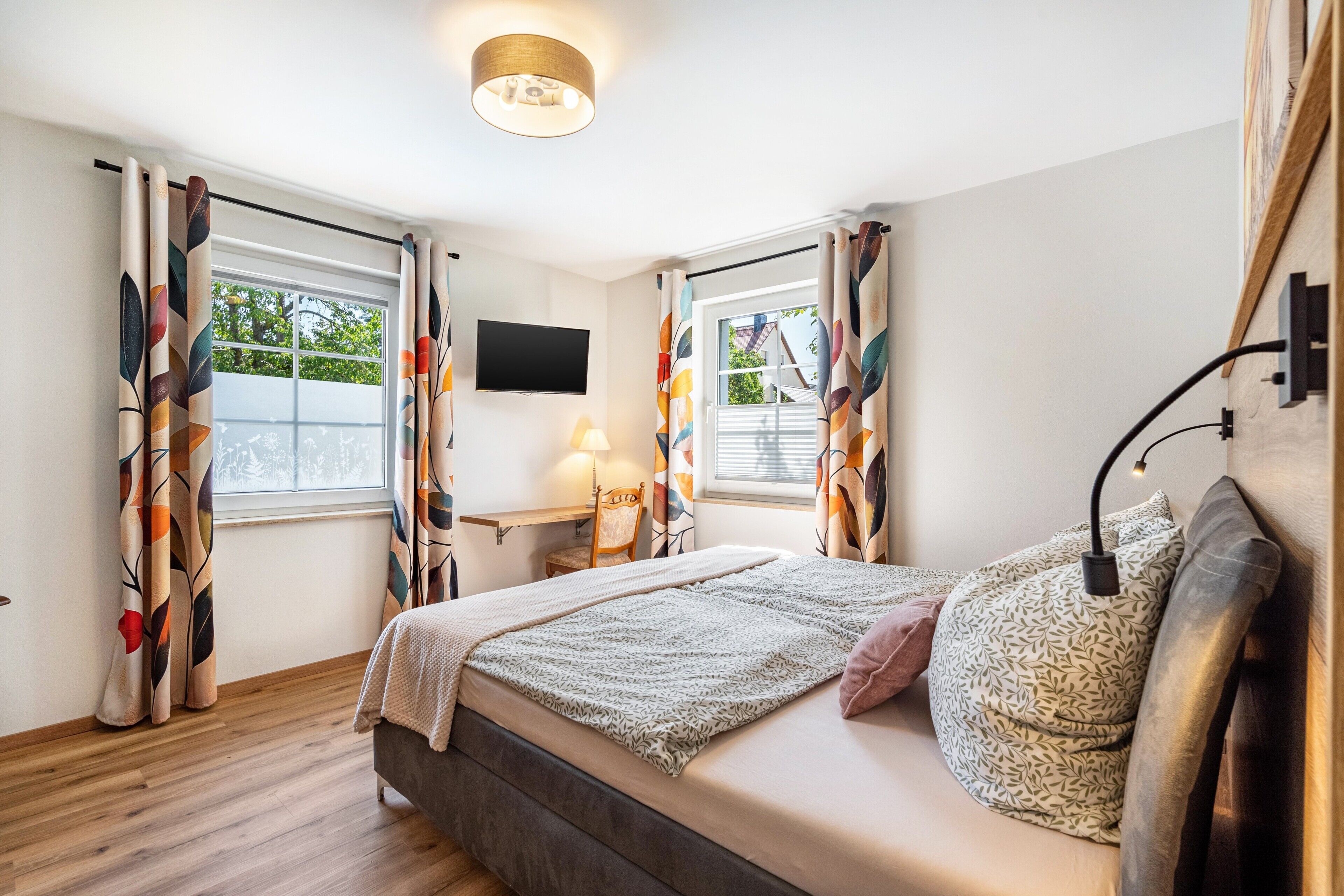 Een slaapkamer met een bed, bureau, stoel, televisie en een raam met gordijnen.