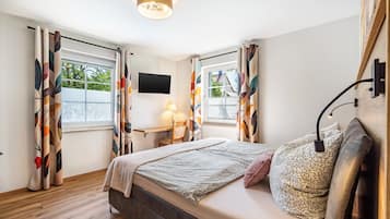 Een slaapkamer met een bed, bureau, stoel, televisie en een raam met gordijnen.