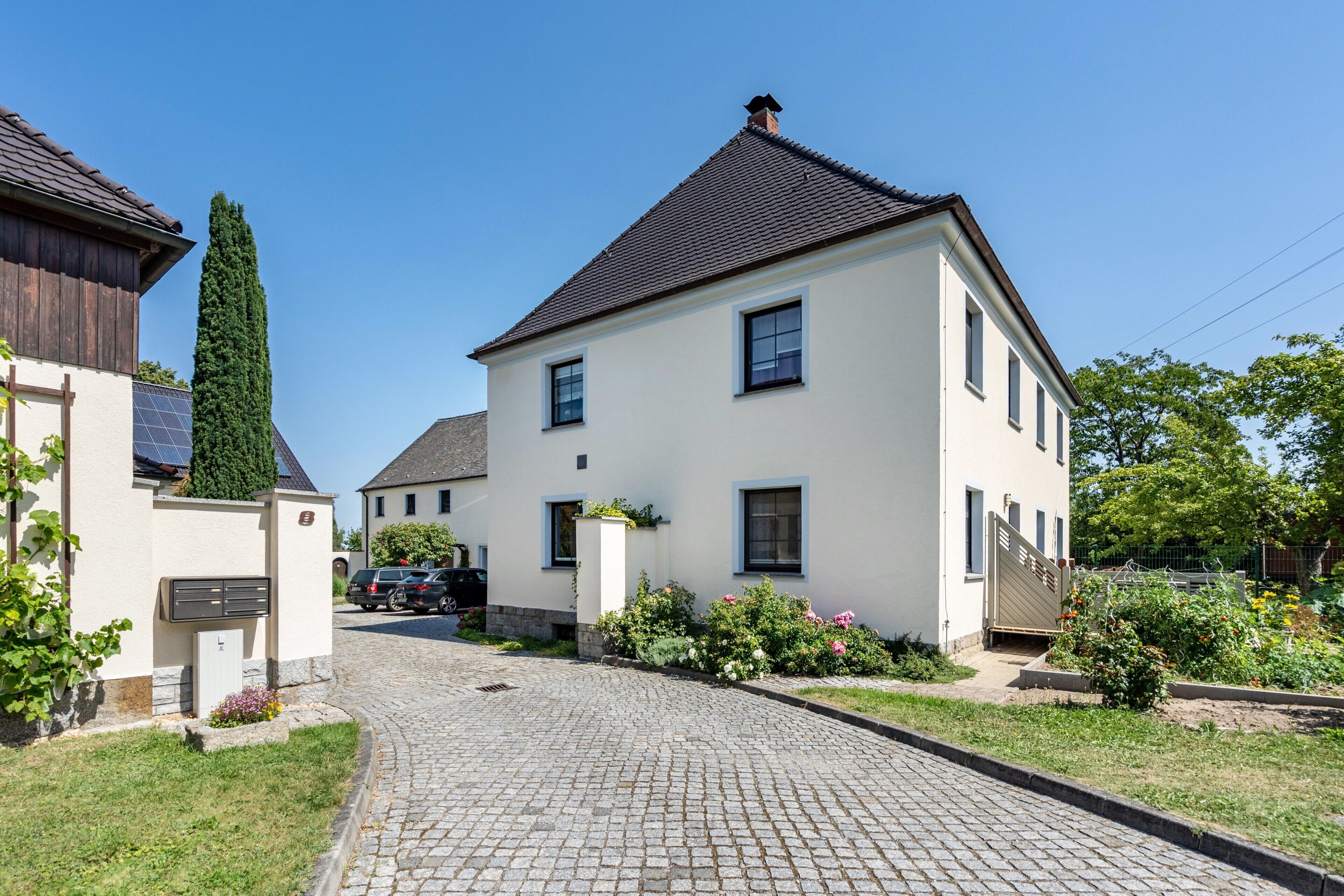 Une maison à deux étages avec une allée pavée et un jardin fleuri.