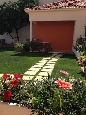 A well-maintained garden with a paved pathway leading to a building with a red door.