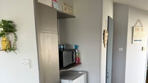 A compact kitchen with a white refrigerator, a microwave, and a small shelf with cleaning supplies. - Beautiful 3 Bed, Sleeps 6, Wifi, Pet Friendly (Bridlington)