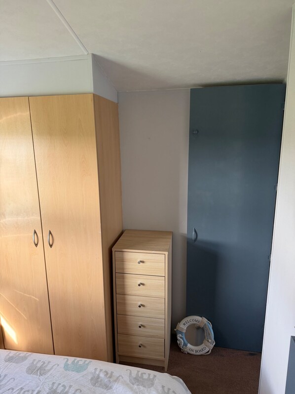 A bedroom with a bed, a wooden wardrobe, a small dresser, a blue door, and a welcome mat on the floor.