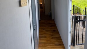 A hallway with a wooden floor leading to a room with a view of a grassy field. A sign on the wall reads "ONE TO THE BEACH". - Beautiful 3 Bed, Sleeps 6, Wifi, Pet Friendly (Bridlington)