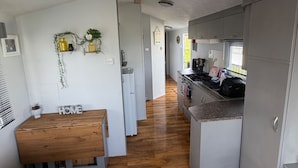 A modern kitchen with a central island, a dining area with a wooden bench, and a living space with a sofa and a rug. - Beautiful 3 Bed, Sleeps 6, Wifi, Pet Friendly (Bridlington)
