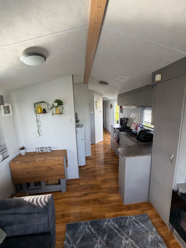 Una cocina moderna con una isla central, un comedor con un banco de madera y una sala de estar con un sofá y una alfombra.