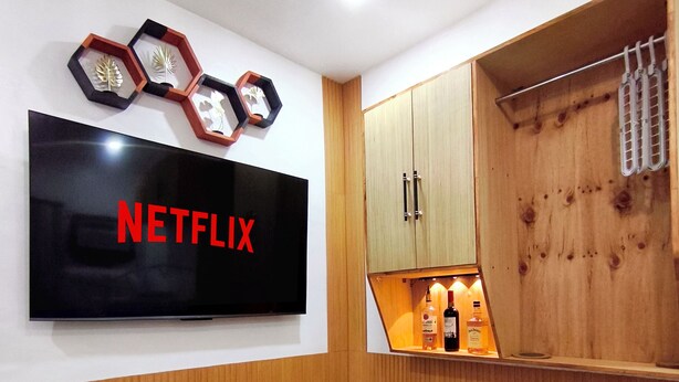 A modern room with a black marble table, a TV mounted on the wall displaying the Netflix logo, wooden cabinets, and a small shelf with bottles. - Cozy Studio Near Clark International Airport, Philippines (Mabalacat City)