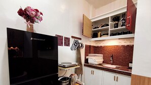 A compact kitchen with a black refrigerator, a microwave, a coffee maker, and a wooden table. There is a vase with flowers on the wall and a cabinet with kitchen utensils. - Cozy Studio Near Clark International Airport, Philippines (Mabalacat City)
