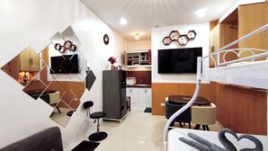 A compact hotel room with a bunk bed, a sofa, a small kitchen area, and a TV mounted on the wall. - Cozy Studio Near Clark International Airport, Philippines (Mabalacat City)